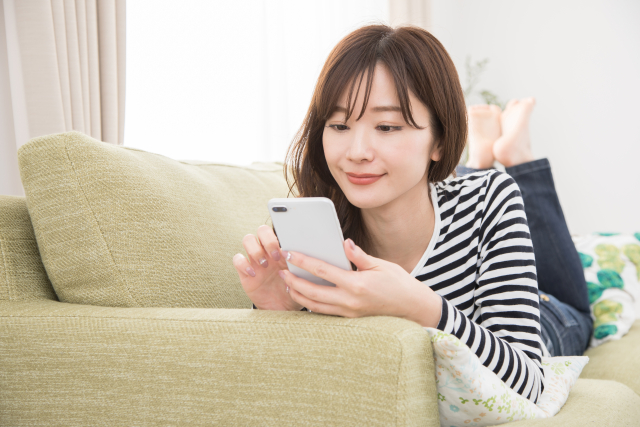 ソファーに寝ころびながらスマホをいじる女性