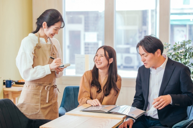男女のお客様からオーダーを取る女性のカフェスタッフ