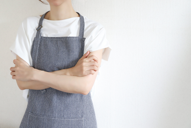 腕を組むエプロン姿の女性の手元