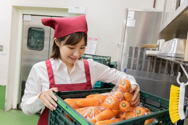 スーパーの裏で届いたニンジンを確認する女性店員