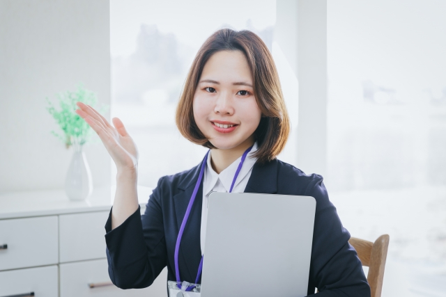 笑顔を浮かべて紹介のポーズを取るスーツの女性