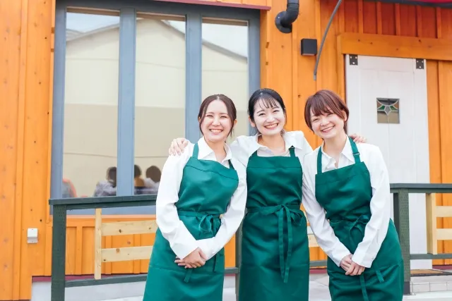 お店の前で肩を組む3人の女性スタッフ