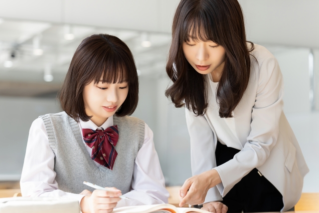 勉強する女子生徒とマンツーマンで指導する女性講師