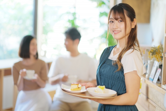 お客様のところへデザートを運ぶカフェの女性スタッフ