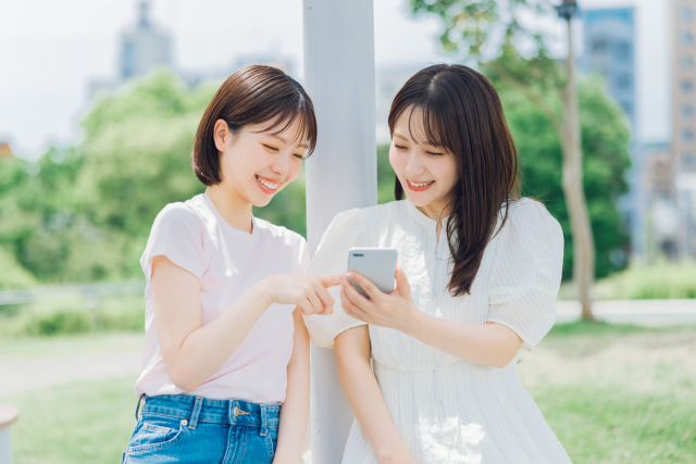 屋外で一緒にスマートフォンを見る二人の女性