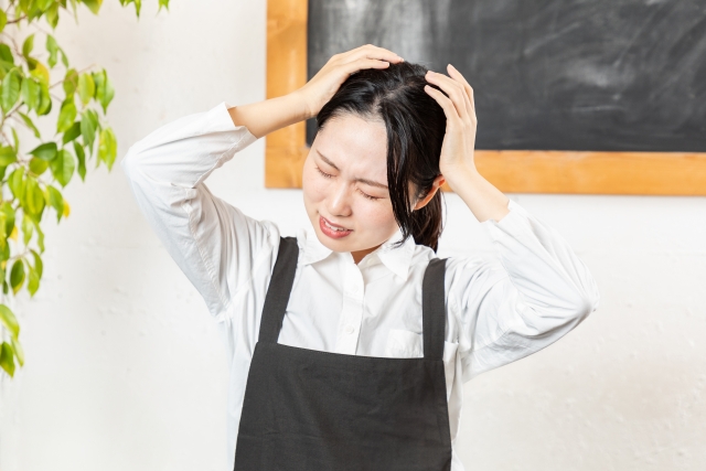 両手で頭を抱えるカフェ店員の女性