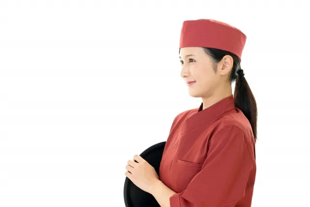 えんじ色の制服に身を包みトレーをわきに抱える女性スタッフ