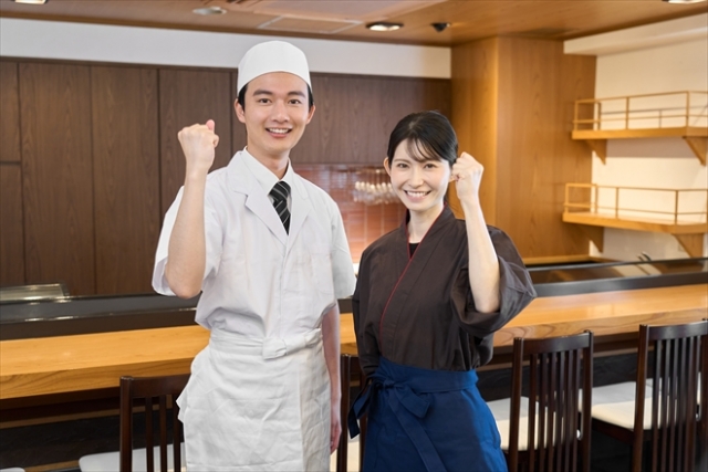 笑顔でこちらにガッツポーズを向けるすし屋で働く男女スタッフ