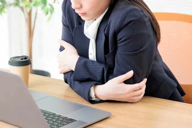 冷房によって冷えた体をさするスーツ姿の女性
