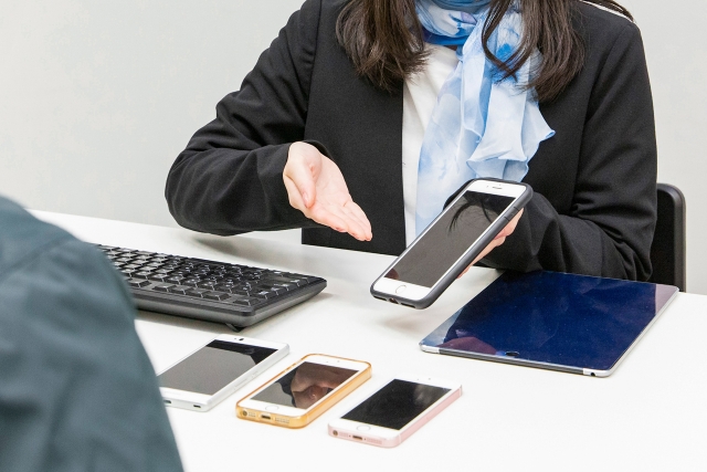 いくつかの種類のスマートフォンを並べてお客様にご案内する女性販売員の手元