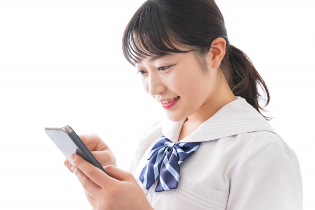 携帯を見ながら微笑むポニーテールの女子高校生
