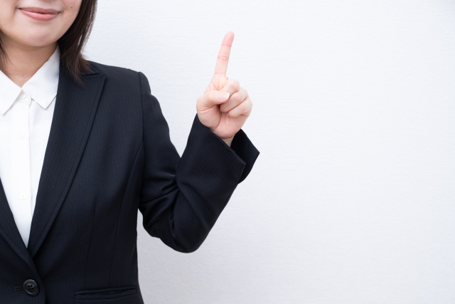 人差し指を立てるスーツの女性の手元
