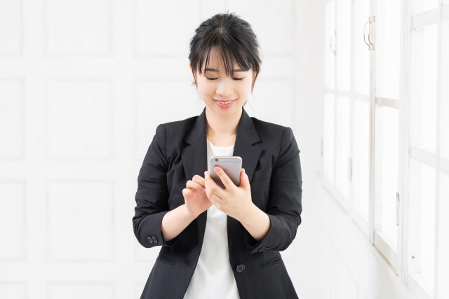 笑顔でスマホを操作するスーツの女性